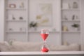 Hourglass with red flowing sand on white table against blurred background Royalty Free Stock Photo