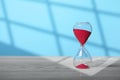 Hourglass with red flowing sand on white wooden table against light blue background, space for text Royalty Free Stock Photo