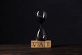 Hourglass or sandglass on cube wooden block with alphabets VAT, Value Added Tax on wood table Royalty Free Stock Photo