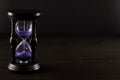 Hourglass sandglass with purple sand on the wooden table, front view. Royalty Free Stock Photo