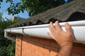 House asbestos roof with plastic roof gutter pipe repair. Contractor hand repair house roof gutter