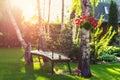 House backyard garden with bench, hanging blossoming flowerswatering hose anf trees. Warm summer or autumn evening sunset time