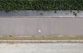 House boundary wall consisting of gray plaster, stripes of metal fence and evergreen hedge above. Porphyry sidewalk and paved road