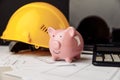 House building costs concept. Safety helmet and piggy bank with blueprint, calculator and laptop Royalty Free Stock Photo