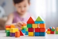House built of colorful wooden kids cubes. Toddler is sitting on the floor of defocused background with copy space Royalty Free Stock Photo