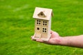 House in caring female hands. Man holding wooden model house in hands on grass background.