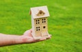 House in caring female hands. Man holding wooden model house in hands on grass background.