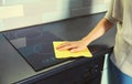 House cleaning concept - woman holding dry microfiber rag wiping the glass surface induction cooker and kitchen countertop from