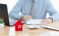 A House on desk envelope with man signing purchase documents in background. while hand complete the insurance policy, rental