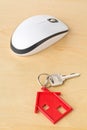 House door key with red house key chain pendant and computer mouse on wooden desk Royalty Free Stock Photo