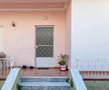 A house entrance stairs to a small terrace, a white door on pink and white walls.