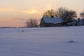 House and farm buildings among snowy fields, on a hill at sunset and with snow falling..