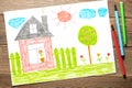 A house, a fence, flowers and an apple tree. Children's drawing on paper. Wooden table with markers Royalty Free Stock Photo