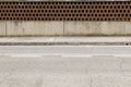 House fence made of low concrete wall and earthenware tiles with an empty circle. Cement sidewalk and asphalt street in front.