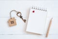 House key with home keyring, blank notebook and pencil on white wood table background Royalty Free Stock Photo
