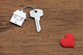 House key with home keyring decorated with mini red heart on wood texture background, sweet home concept Royalty Free Stock Photo