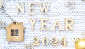 House key with keychain cottage on cozy festive knitted background with stars, bokeh. Happy New Year 2024 wooden letters, greeting