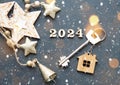 House key with keychain cottage on festive background with stars, lights of garlands. New Year 2024 wooden letters, greeting card