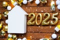 House key with tiny figure of home mock up on festive brown wooden background, lights of garlands. New Year 2025 wooden letters,