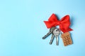 House keys with trinket and bow on color background, top view.