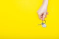 House keys with trinket in female hand on color background, top view with copy space. House key on yellow background. Minimal flat Royalty Free Stock Photo