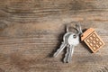 House keys with trinket on wooden background, top view.