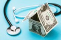 House made of dollars and a medical stethoscope on a blue background. Concept on the cost of a call to a doctor at home Royalty Free Stock Photo
