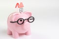 House maintenance budget, cost, savings or mortgage home loan concept, miniature house on pink piggy bank wearing glasses on white Royalty Free Stock Photo