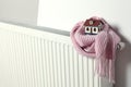 House model wrapped in pink scarf on radiator, space for text. Winter heating efficiency Royalty Free Stock Photo