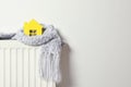 House model wrapped in scarf on radiator, space for text. Winter heating efficiency Royalty Free Stock Photo