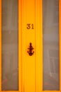 House number 31 on a bright orange wooden front door with glass and an anchor as  door knocker Royalty Free Stock Photo