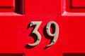 House number 39 on a bright red wooden front door with strong shadows