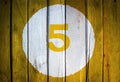 House number or calendar date in white circle on yellow toned wooden door background. Number five 5