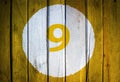 House number or calendar date in white circle on yellow toned wooden door background. Number nine 9 Royalty Free Stock Photo