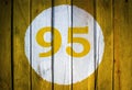 House number or calendar date in white circle on yellow toned wooden door background. Number ninety five 95