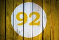House number or calendar date in white circle on yellow toned wooden door background. Number ninety two 92 Royalty Free Stock Photo