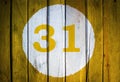 House number or calendar date in white circle on yellow toned wooden door background. Number thirty one 31