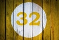 House number or calendar date in white circle on yellow toned wooden door background. Number thirty two 32 Royalty Free Stock Photo