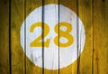 House number or calendar date in white circle on yellow toned wooden door background. Number twenty eight 28 Royalty Free Stock Photo