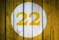 House number or calendar date in white circle on yellow toned wooden door background. Number twenty two 22 Royalty Free Stock Photo