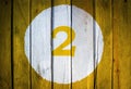 House number or calendar date in white circle on yellow toned wooden door background. Number two 2 Royalty Free Stock Photo