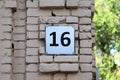 House number sixteen. Black lettering on a white metal plate on an old brick wall Royalty Free Stock Photo