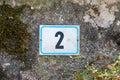 House number two. Black lettering with blue frame on a white metal plate nailed to a wall Royalty Free Stock Photo