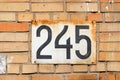 House number 245 two hundred and forty five a rusty white metal plate on an old brick wall Royalty Free Stock Photo