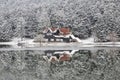 House and pine trees under snow by lake with reflection Royalty Free Stock Photo