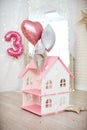 house for playing with dolls with a pink roof stands on the floor in a bright room decorated with balloons