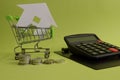 House put in a shopping cart and coins, calculator on the desk. Royalty Free Stock Photo