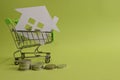 House put in a shopping cart and coins on the desk. Royalty Free Stock Photo