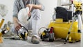 House renovation concept, construction worker holds in hands helmet and safety headphones, air compressor and construction tools