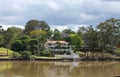 House on the river in Queensland Australia with palms and tall gumn trees under a stormy sky in spring